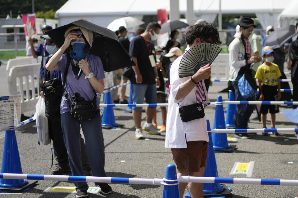 Visitors use fans and umbrellas in the heat outside the Fuji International Speedway, the finish for the women's cycling road race that is underway, at the 2020 Summer Olympics, Sunday, July 25, 2021, in Oyama, Japan. (AP Photo/Christophe Ena)