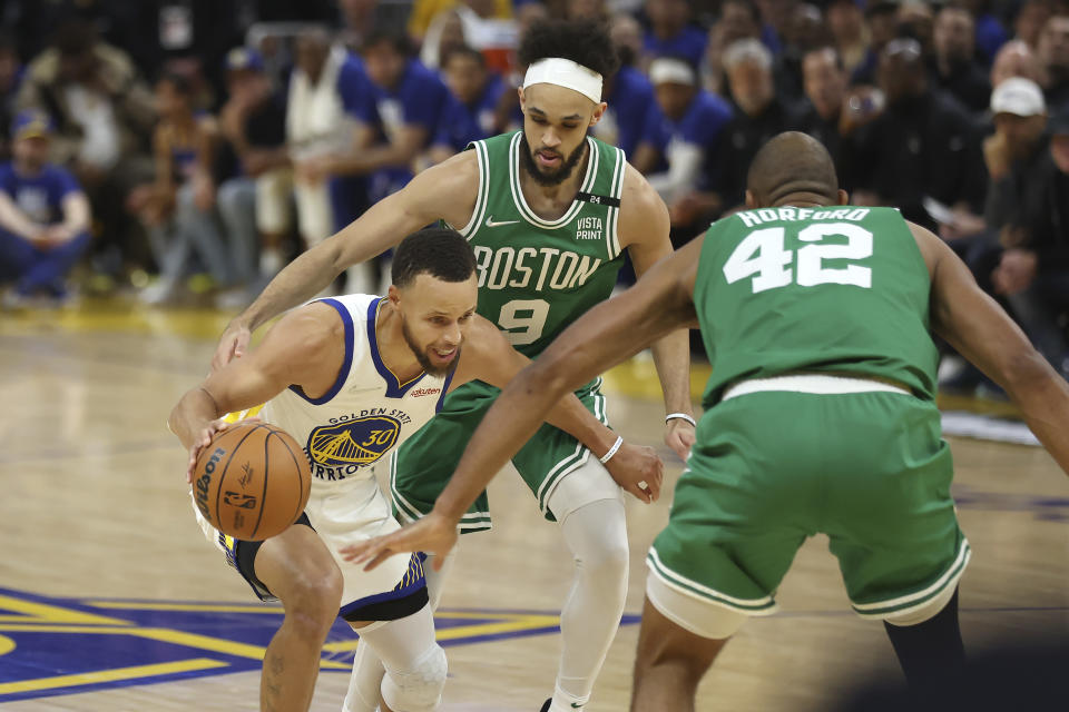 Golden State Warriors guard Stephen Curry (30) is defended by Boston Celtics center Al Horford (42) and guard Derrick White (9) during the first half of Game 1 of basketball's NBA Finals in San Francisco, Thursday, June 2, 2022. (AP Photo/Jed Jacobsohn)