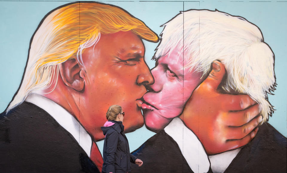 A woman passes a mural painted on a derelict building in Bristol, showing Donald Trump sharing a kiss with Boris Johnson (Getty Images)