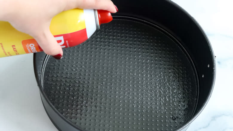 a springform pan being greased with cooking spray
