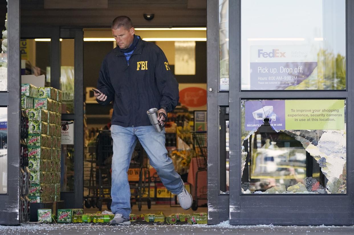 An FBI agent steps over soft drink bottles and broken glass as he walks through a damaged entrance at a Kroger grocery store Friday, Sept. 24, in Collierville, Tenn. 