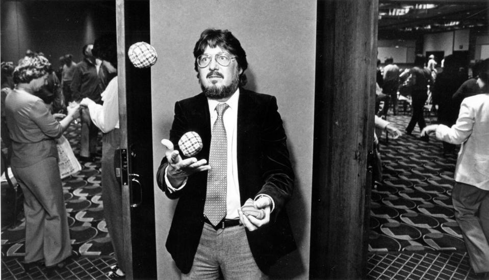 A man in suit and tie juggles outside a hotel ballroom.