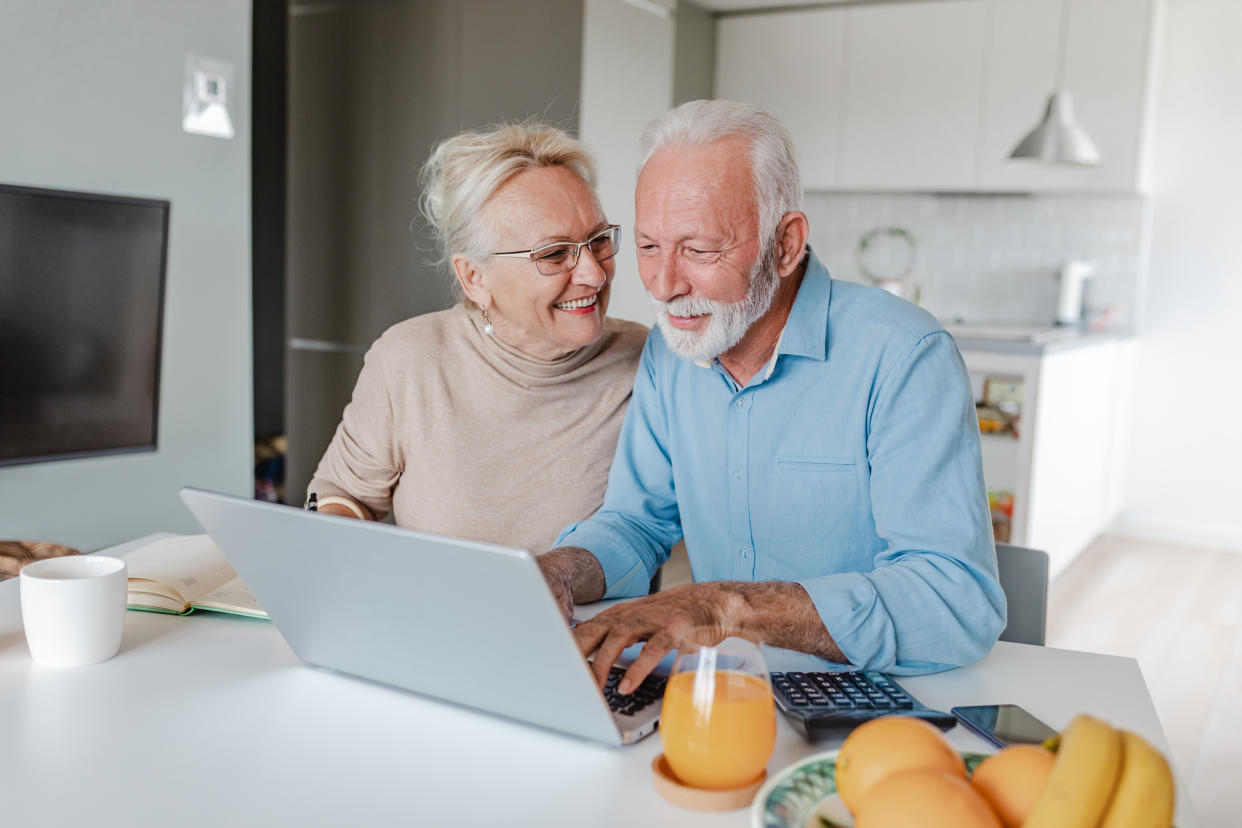 A senior couple is at home, they are sitting at the table and using a laptop pension