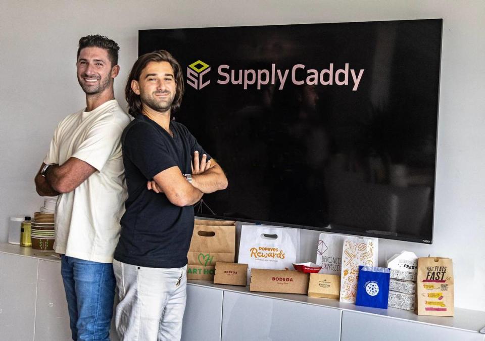 SupplyCaddy co-founders Zachary Stein and Bradley Saveth posed next to a display of different packaging and disposable products their company makes for the food service industry.