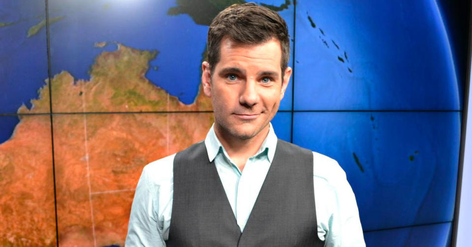 Nate Byrne stands in front of a screen showing the globe, wearing a grey vest over a light blue shirt, before his transformation.