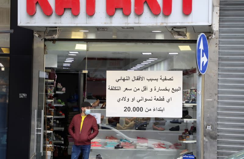 A man stands at the entrance of a shop with a sign in Arabic reading, "Liquidation for closure" in Beirut