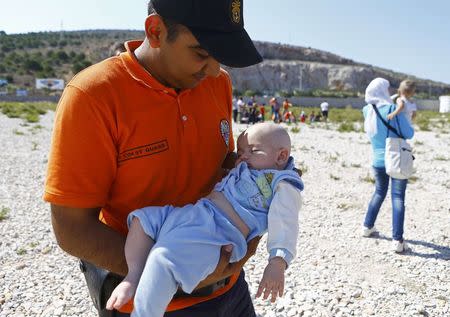 A member of the Turkish coast guards carries a baby of Syrian migrant on the shore in Cesme, near the Aegean port city of Izmir, Turkey, August 11, 2015. REUTERS/Osman Orsal