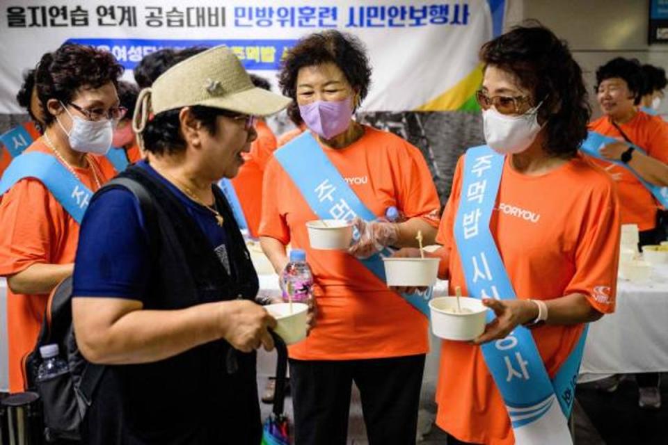 A civilian is offered snacks and bottled water during a civil defence drill against possible artillery attacks by North Korea, in a subway station in Seoul on 23 August 2023 (AFP via Getty Images)