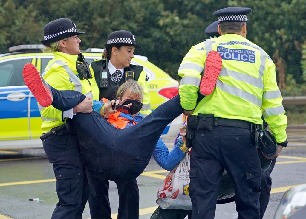 Police officers detain a protester from Insulate Britain occupying a roundabout leading from the M25 motorway to Heathrow Airport in London (PA) (PA Wire)