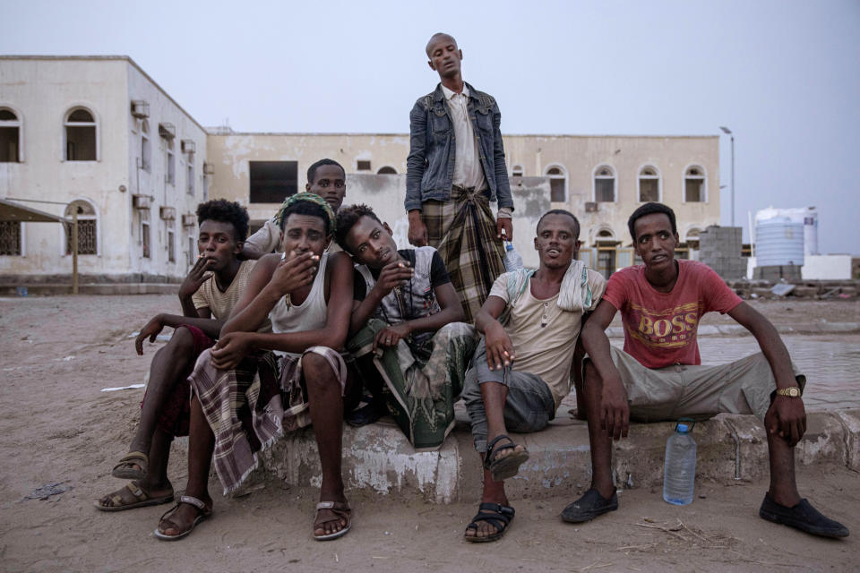 In this July 21, 2019 photo, Ethiopian migrants sit together and smoke, as they take shelter in the "22nd May Soccer Stadium," destroyed by war, in Aden, Yemen. Over the summer, the stadium became a temporary refuge for thousands of migrants. At first, security forces used it to house migrants they captured in raids. Other migrants showed up voluntarily, hoping for shelter. The IOM distributed food at the stadium and arranged voluntary repatriation back home for some. The soccer pitch and stands became a field of tents, with clothes lines strung up around them. (AP Photo/Nariman El-Mofty)