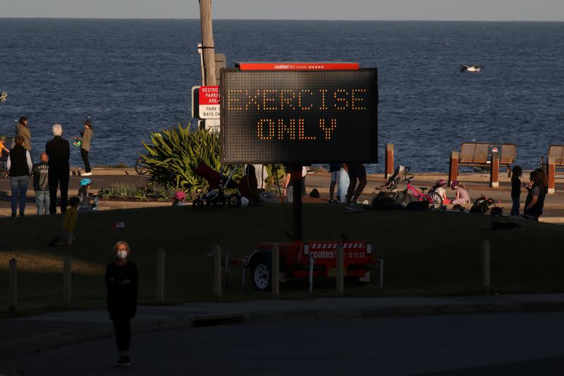 A woman wearing a protective face mask walks past a sign reminding people of outdoor limitations in Sydney