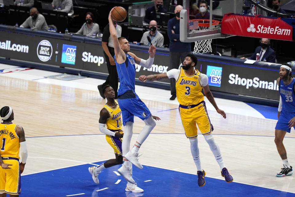 Dallas Mavericks center Kristaps Porzingis (6) gets past Los Angeles Lakers' Dennis Schroeder (17) and Anthony Davis (3) for a dunk during the first half of an NBA basketball game in Dallas, Thursday, April 22, 2021. (AP Photo/Tony Gutierrez)