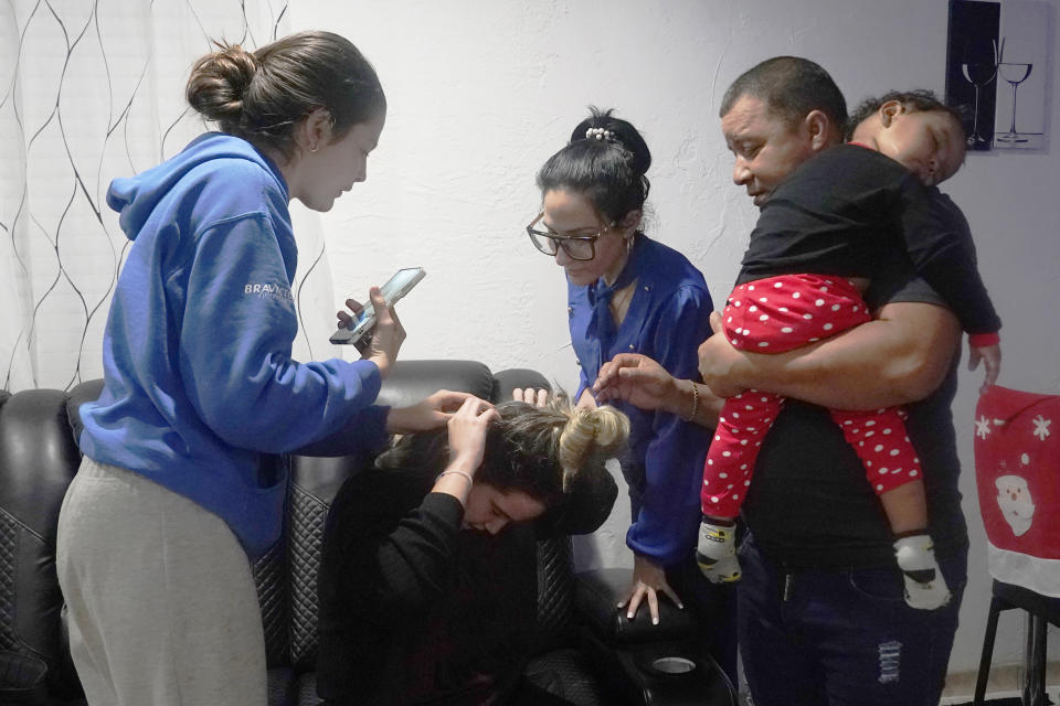 Merlyn Rolo Gonzalez shows her stitches to her sister Melanie, left, at the home of family friends Solanche Rodriguez and Walfrido Fuentes, in Daytona, Florida, Tuesday, Jan. 3, 2023. Fuentes holds Melanie's daughter, Madisson. The child and the young women recently arrived in the U.S., after a three-week journey through Central America and Mexico. During the trip, the sisters were packed in a vehicle overnight with other migrants when it slipped and flipped over 10 times. (AP Photo/Marta Lavandier)