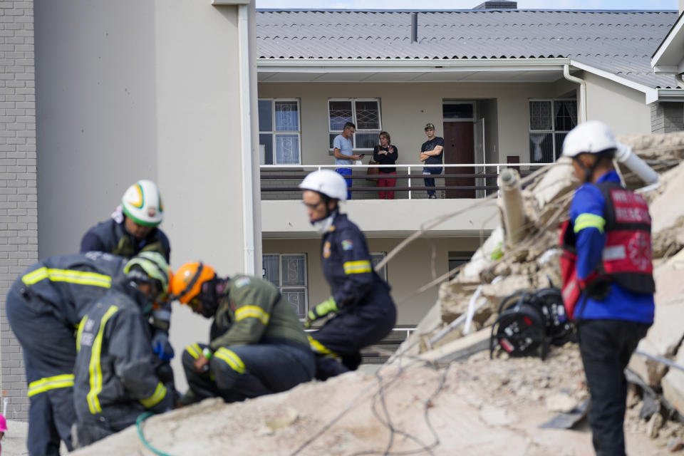 Residents watch rescue workers search the site of a building collapse in George, South Africa, Wednesday, May 8, 2024. Rescue teams are searching for dozens of construction workers missing after a multi-story apartment complex collapsed in the coastal city have brought out more survivors as the operation entered a second night of desperate work to find anyone alive in the mangled wreckage. (AP Photo/Jerome Delay)