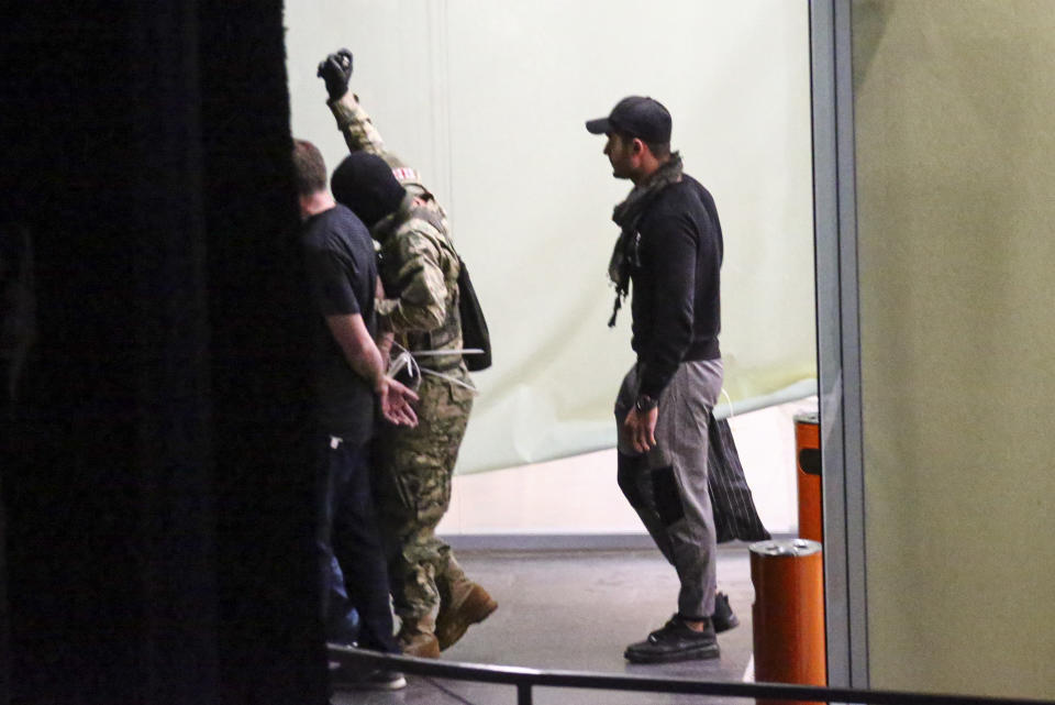 A gunman with a weapon in a hand, left, escorts three police officers, who surrendered themselves as hostages, out of the bank building as the fourth police officer with a bag follows them, in the town of Zugdidi in western Georgia, Wednesday, Oct. 21, 2020. Authorities in the ex-Soviet republic of Georgia say an armed assailant has taken hostages at a bank. Local media reported that up to 19 hostages could be inside the bank. The Georgian Interior Ministry didn't immediately comment on how many people were taken hostage Wednesday in the western town of Zugdidi or what demands their captor had made. (AP Photo/Zurab Tsertsvadze)