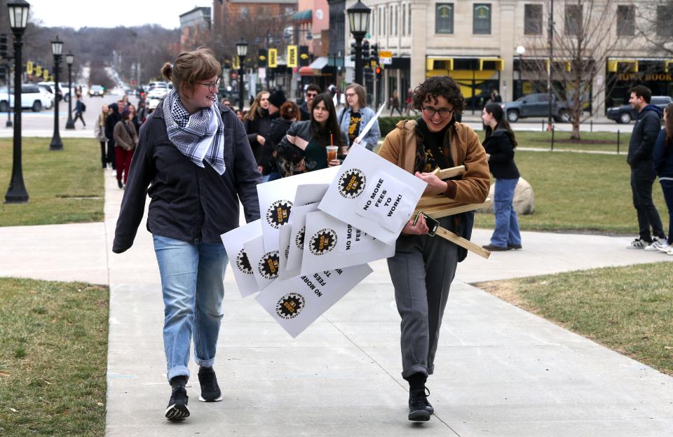 Hannah Zadeh, right, carries signs for the COGS UE Local 896, representing University of Iowa graduate student workers, protest of graduate student fees Tuesday, March 5, 2024 on the University of Iowa campus in Iowa City, Iowa.