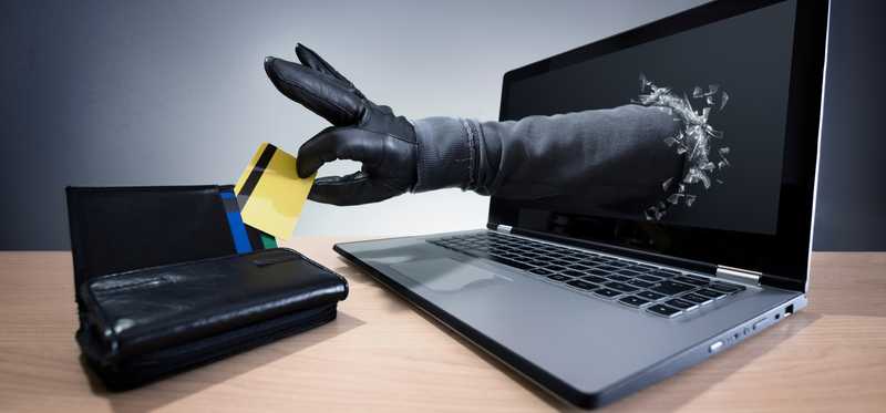 Gloved hand reaches through laptop screen a steals a credit card.