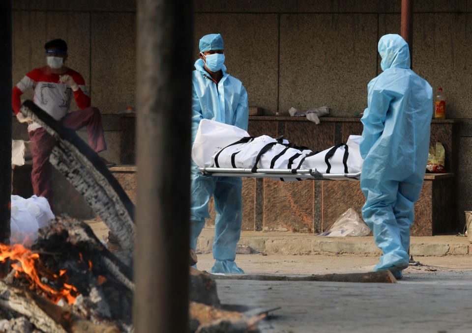 Health workers wearing Personal Protective Equipment (PPE) carry the body of a covid19 victim during the mass cremation at Dwarka crematorium.