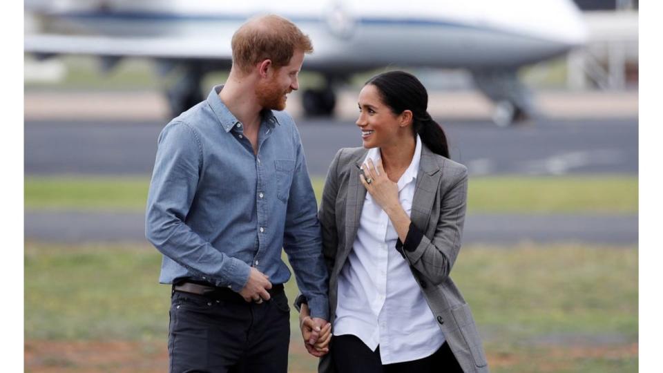 Prince Harry talking to Meghan Markle as they walk outside at an airport