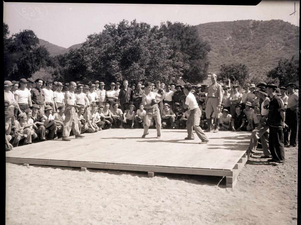 A black and white photo of two men boxing in front of a large crowd.