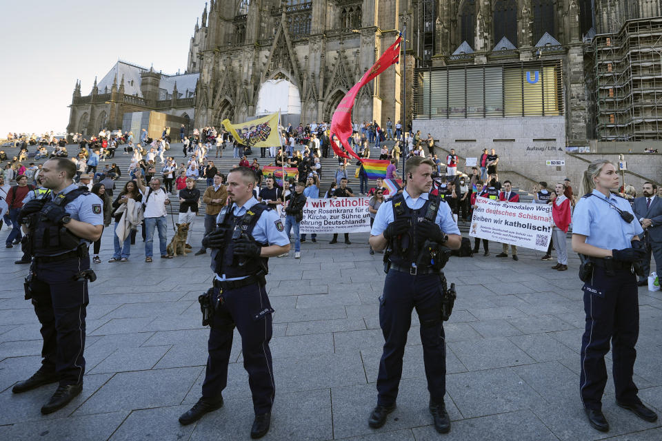 A demonstration against a public blessing ceremony is secured by police in front of the Cologne Cathedral in Cologne, Germany, Wednesday, Sept. 20, 2023. Several Catholic priests held a ceremony blessing same-sex and also re-married couples outside Cologne Cathedral in a protest against the city's conservative archbishop, Cardinal Rainer Maria Woelki. (AP Photo/Martin Meissner)