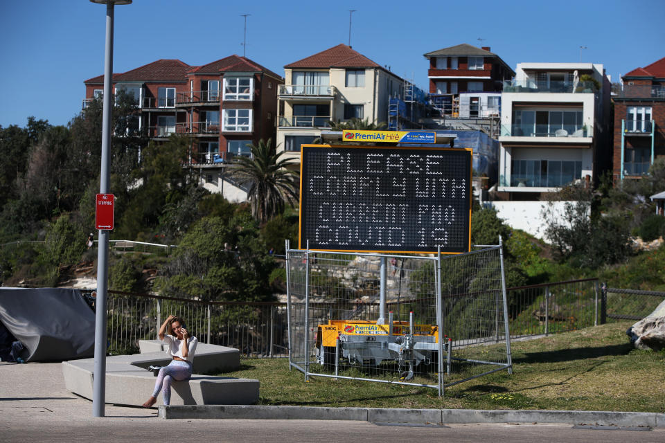 A person sits talking on their phone near a Covid-19 public notice sign at Sydney's Bondi Beach on September 24. 2021.