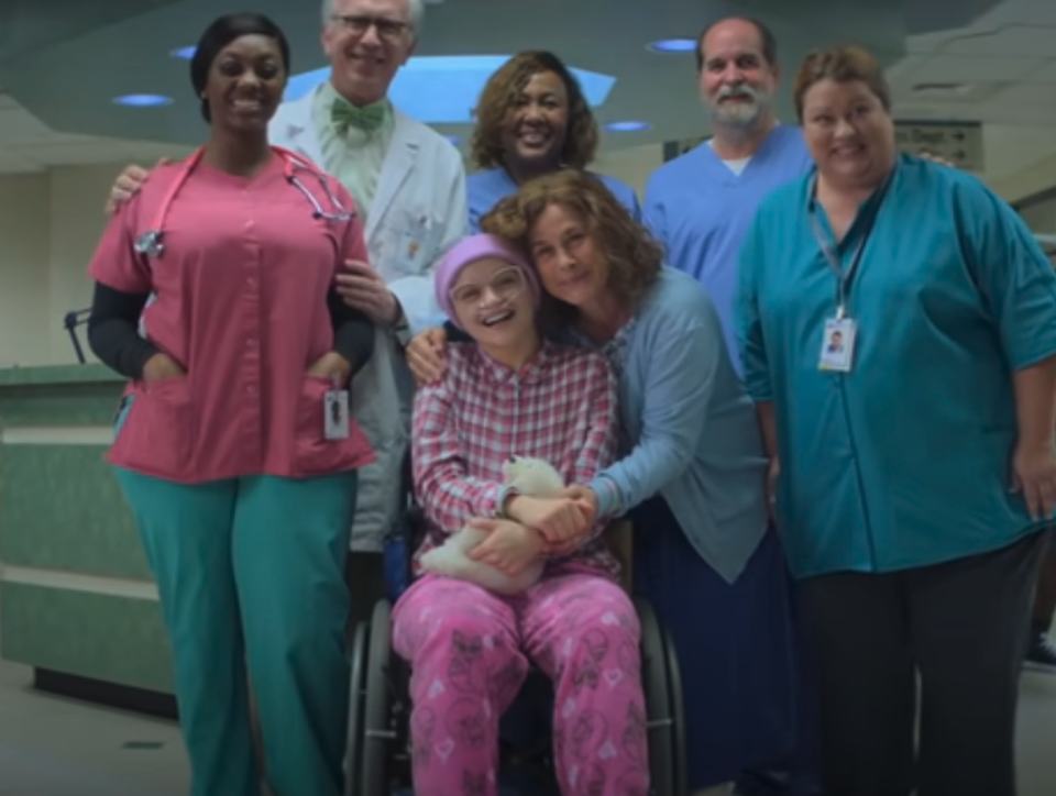 A child in a wheelchair and surrounded by smiling medical professionals and her mother in a hospital