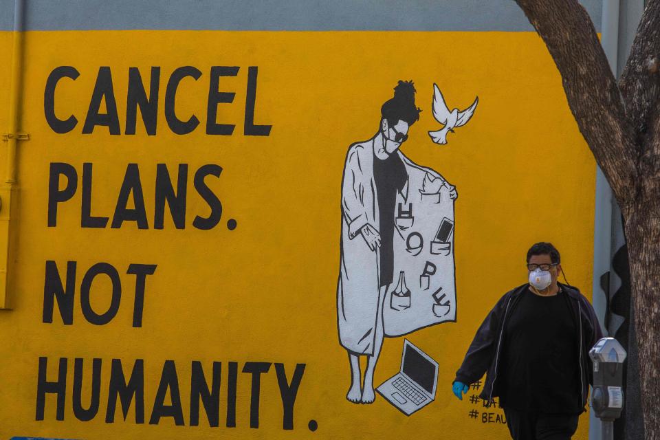 A man wearing gloves and a face mask walks by a mural reading "Cancel Plans Not Humanity" during the coronavirus (COVID-19) pandemic on April 4, 2020 in Los Angeles.