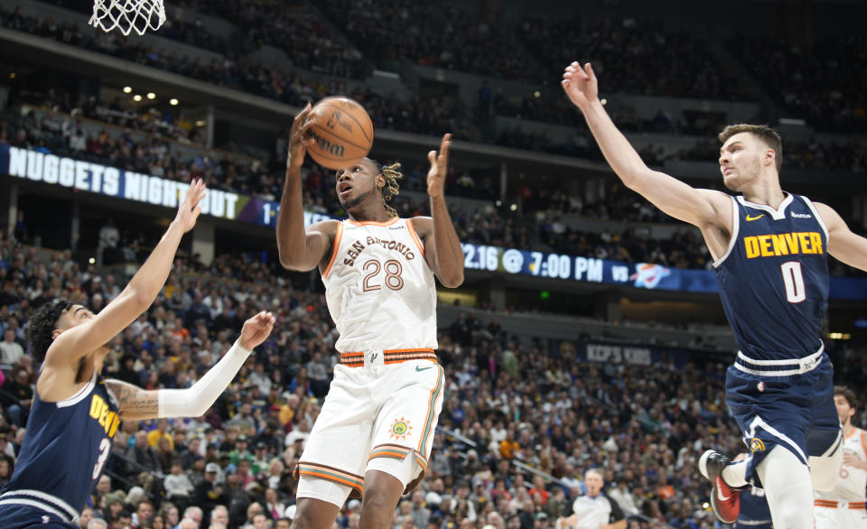 San Antonio Spurs center Charles Bassey, center, drives to the basket between Denver Nuggets guards Julian Strawther, left, and Christian Braun, right, in the first half of an NBA basketball game Sunday, Nov. 26, 2023, in Denver. (AP Photo/David Zalubowski)