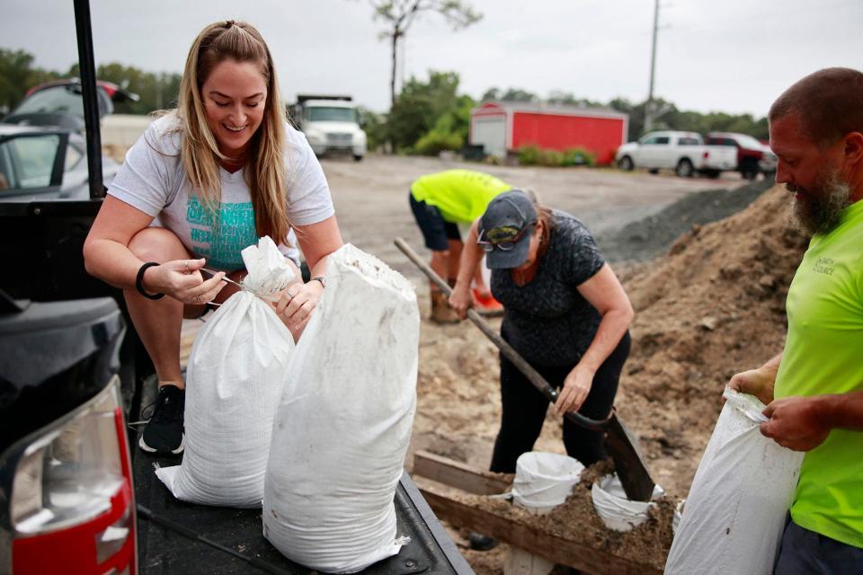 Springfield resident Jamie Lepp, left, ties sandbags alongside Kim Pryor as Earth Source employee Robert Cumberland helps move bags Wednesday at the landscape supply company's operation on North Main Street  in Jacksonville. Earth Source was donating free fill sand as thousands across the region braced for Hurricane Ian. [Corey Perrine/Florida Times-Union]