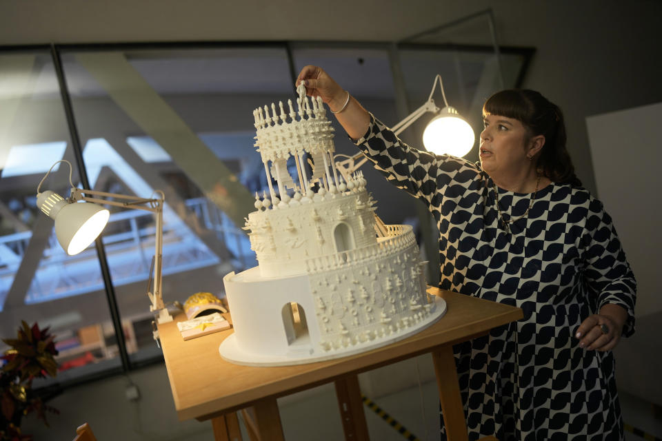 Portuguese artist Joana Vasconcelos places a human figure on the top tier of a model of her 12 meters high and 15 meters wide ceramic wedding cake, at her studio in Lisbon, Friday, Nov. 11, 2022. The Wedding Cake, her most ambitious outdoor project yet, will be erected in the gardens of Waddesdon Manor in southeast England, which hosts weddings. (AP Photo/Armando Franca)