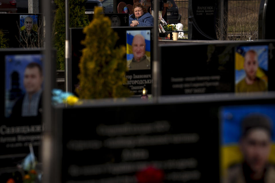 A woman sits behind graves of Ukrainian servicemen and civilians killed during the Russian occupation during a commemoration of the victims at a cemetery in Bucha, Ukraine, Sunday, March 31, 2024. Ukrainians mark the second anniversary of the liberation of Bucha, during which Russian occupation left hundreds of civilians dead in the streets and in mass graves in Bucha during the initial months of the Russian invasion in 2022. (AP Photo/Vadim Ghirda)