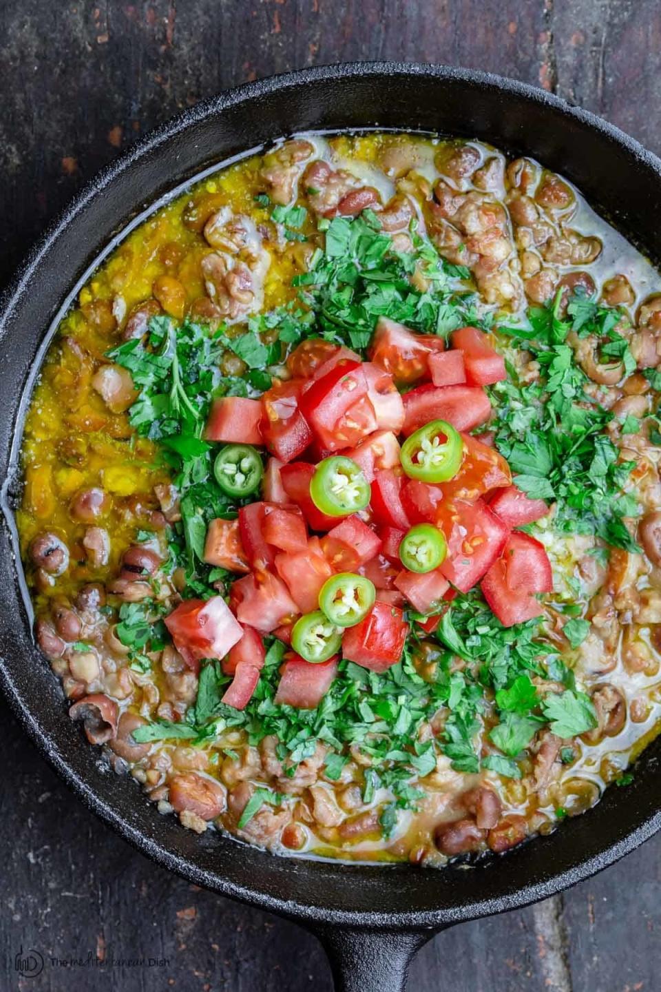 Egyptian fava bean dip in a skillet with tomatoes and herbs.