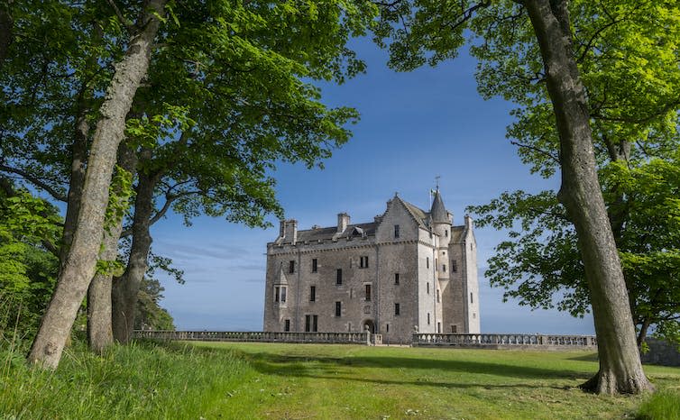 A castle sitting between trees on a bright spring day with a blue sky behind.