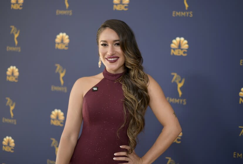 A woman with long, brown hair in a burgundy dress poses smiles at a red carpet.