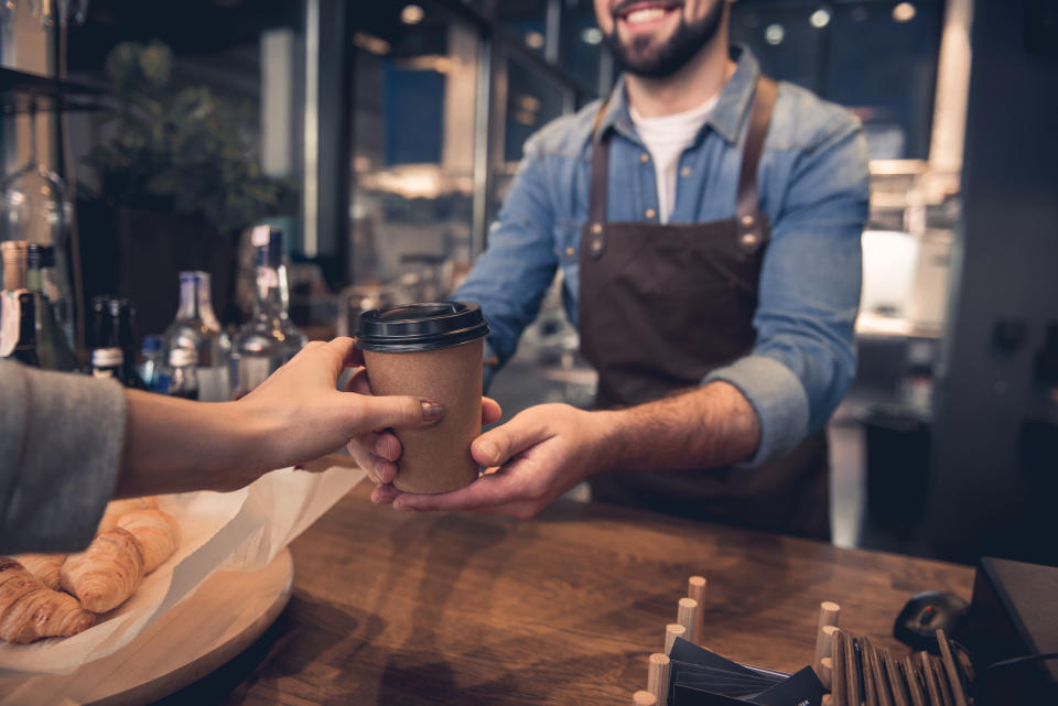 Close up female hand taking cup of hot coffee from barista in confectionary shop. Purchase concept. Growth in private sector fell sharply as cost of living hits consumer firms. Photo: Getty