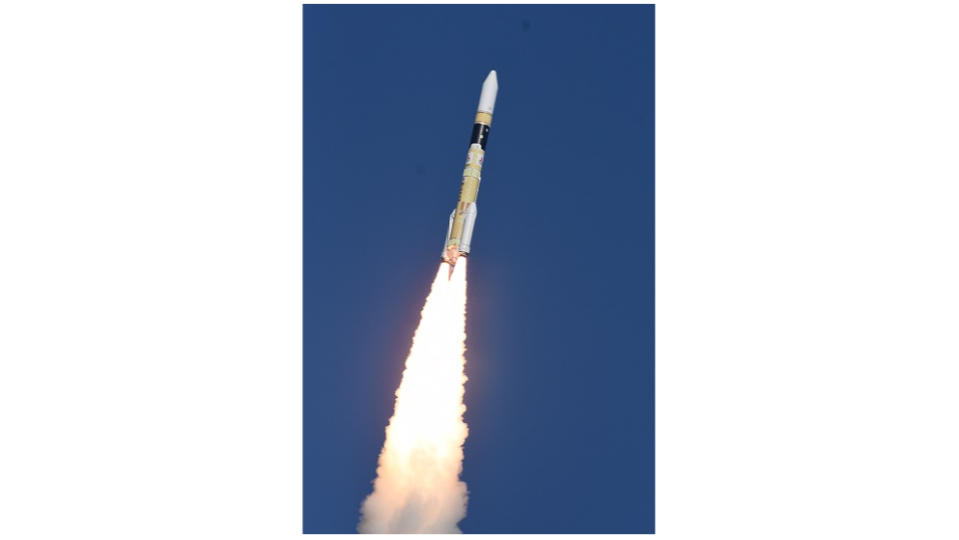 a white, orange and black rocket rises into a clear blue sky.