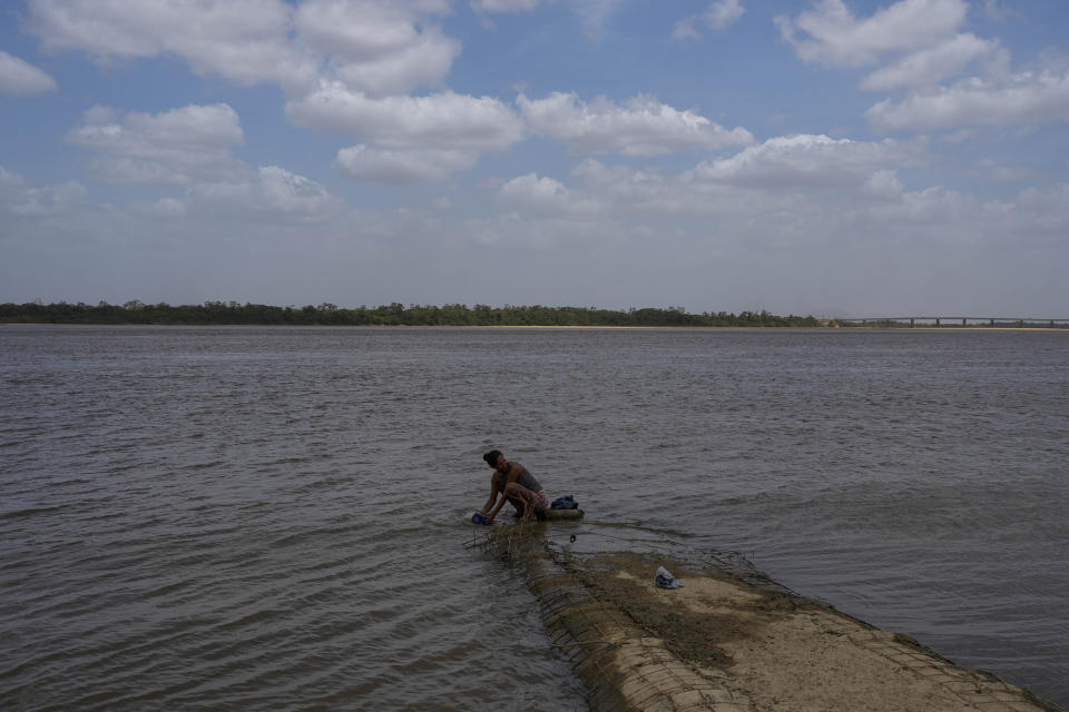 A Venezuelan migrant washes her clothes in the Branco River in Boa Vista, Roraima state, Brazil, Friday, April 7, 2023. (AP Photo/Matias Delacroix)