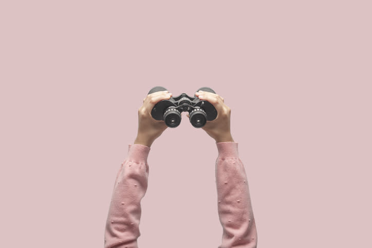 A pair of hands holding a pair of binoculars overhead.