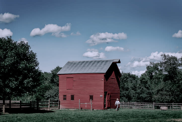 Person walking towards a red barn on a farm under a cloudy sky