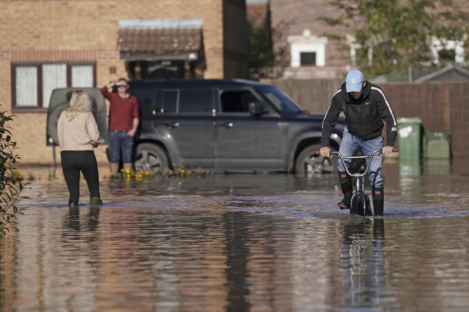 A man tried to cycle after flooding in Retford in Nottinghamshire, Sunday, Oct. 22, 2023, after Storm Babet battered the UK, causing widespread flooding and high winds. (Joe Giddens/PA via AP)