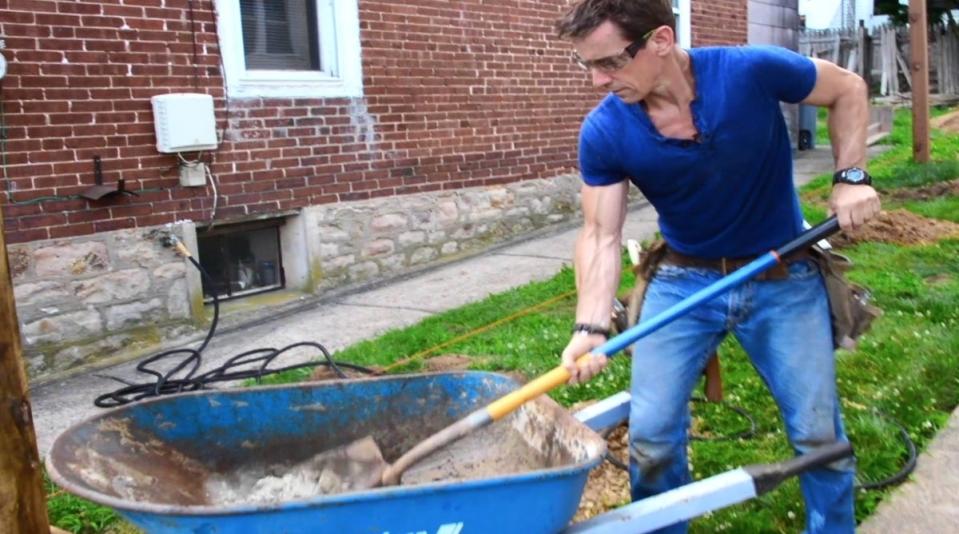 Man mixing concrete in a blue wheelbarrow.