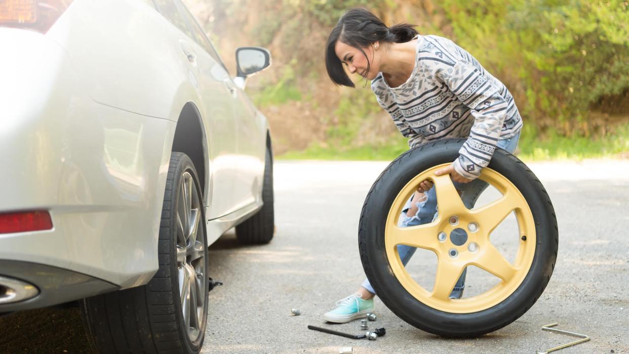 A young hispanic women stranded on the side of the road changing a flat tire.