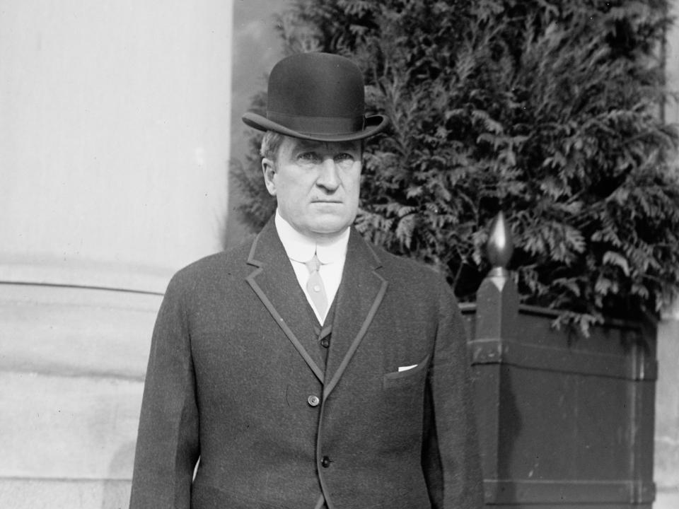 John A. Dix standing outside a building with a stern look on his face while wearing a hat and a black blazer.