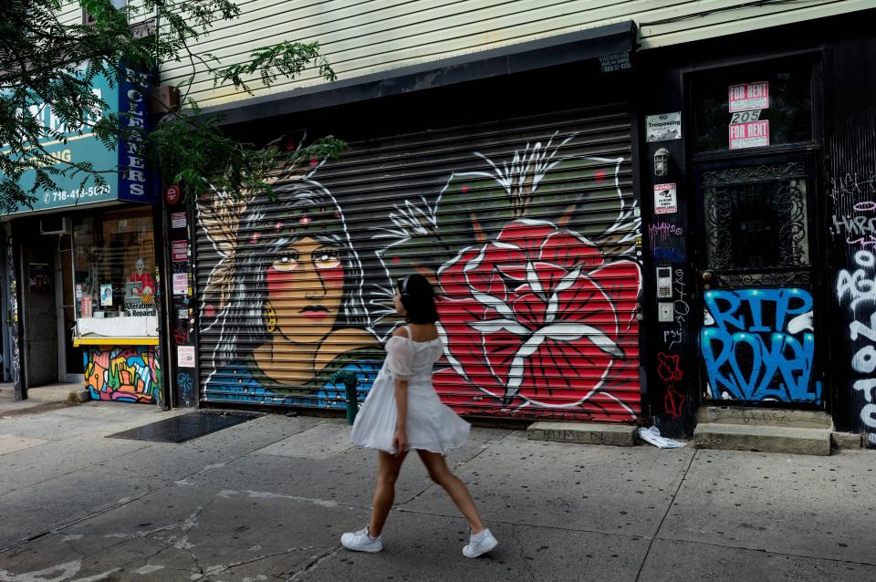 A girl walks on the street, past a graffiti-covered shuttered storefront.
