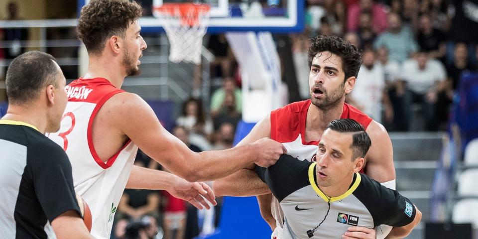 Furkan Korkmaz is held back by a referee as teammates intervene during an altercation during a game.