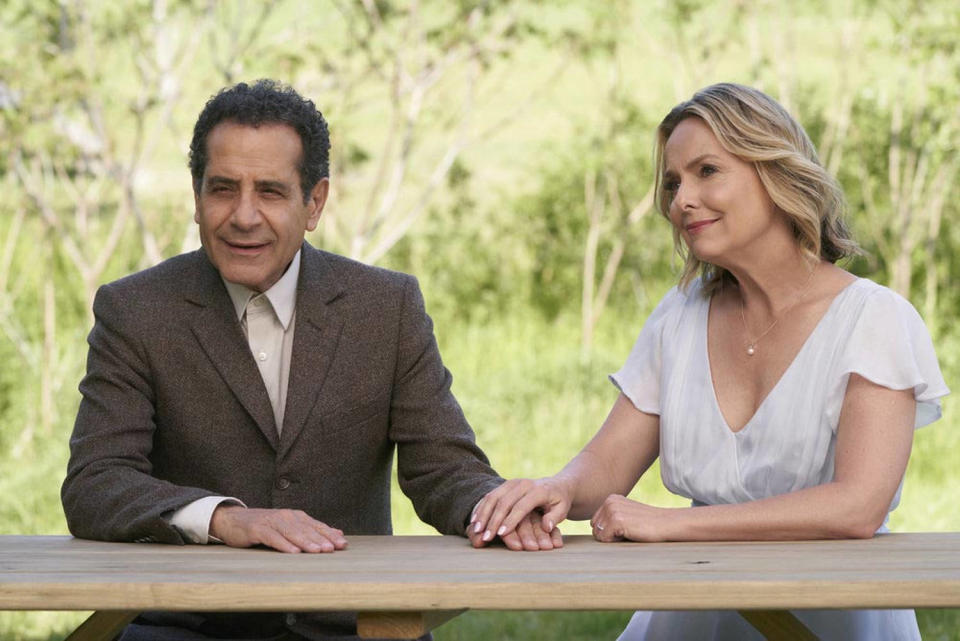 Shalhoub as Adrian Monk in a brown suit sits outside and holds hands with Melora Hardin as Trudy, who is wearing a white dress with a v-neck and flutter sleeves. (Courtesy of Peacock)