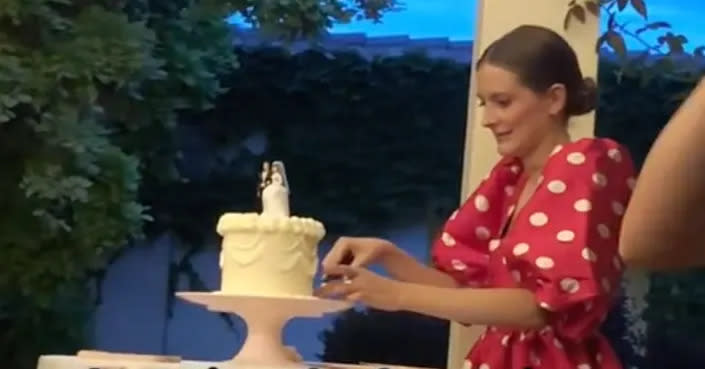 A woman in a spotty dress cuts a wedding cake. 