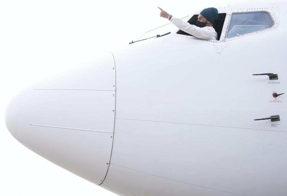 NDP Leader Jagmeet Singh sticks his head out the window of the cockpit of his campaign plane and points ahead.
