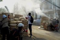 Anti-coup demonstrators sprays fire extinguishers over a barricade during a protests in Yangon